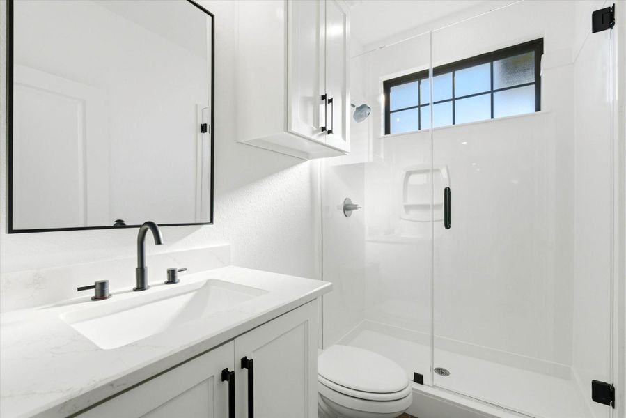 The upstairs bath is complete with a glass-enclosed walk-in shower, frosted window for privacy, and convenient storage above the commode.