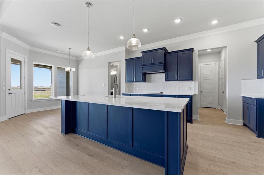Kitchen with blue cabinets, ornamental molding, backsplash, a kitchen island with sink, and hanging light fixtures