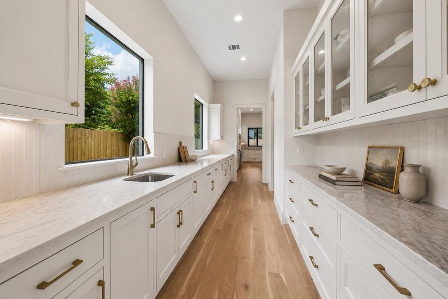 Prep work feels elevated in a massive scullery with extensive cabinetry, a large walk in pantry for dry goods, and a secondary sink tucked beneath a large picture window - already plumbed and ready for a dishwasher install. Glass front uppers, natural stone surfaces, and thoughtfully curated finishes create a clean extension of the main kitchen while keeping everyday essentials organized and out of sight. **Virtually staged**