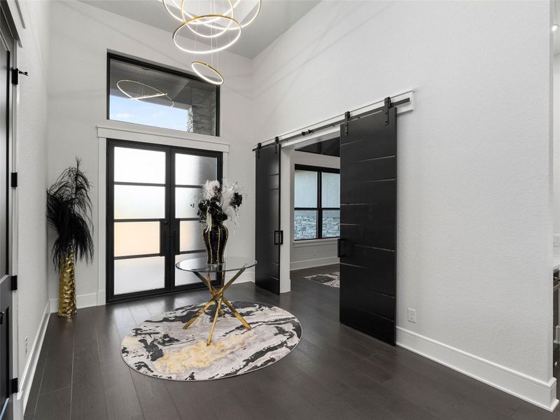 Entrance foyer with a high ceiling, a barn door, plenty of natural light, a chandelier, and dark wood-style floors