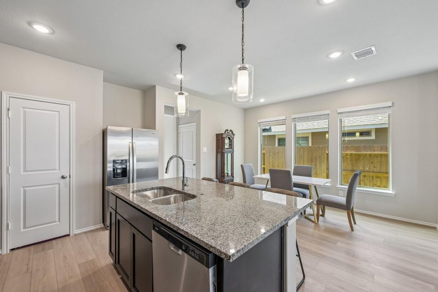 Modern kitchen with a sleek granite island, stainless steel appliances, and an open dining area filled with natural light.