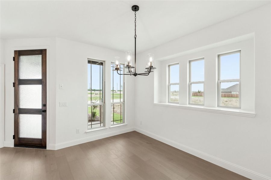 Empty dining room with hardwood floors, black chandelier, multiple windows, and dark wood glass-panel door Empty dining room with hardwood floors, black chandelier, multiple windows, and dark wood glass-panel door