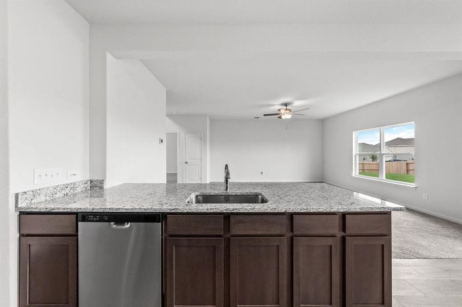 Kitchen featuring dark brown cabinetry, sink, light stone counters, dishwasher, and kitchen peninsula