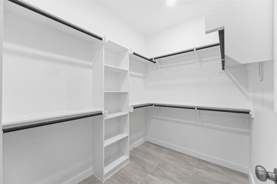 Spacious walk-in closet featuring built-in shelving, multiple hanging rods, and tile flooring