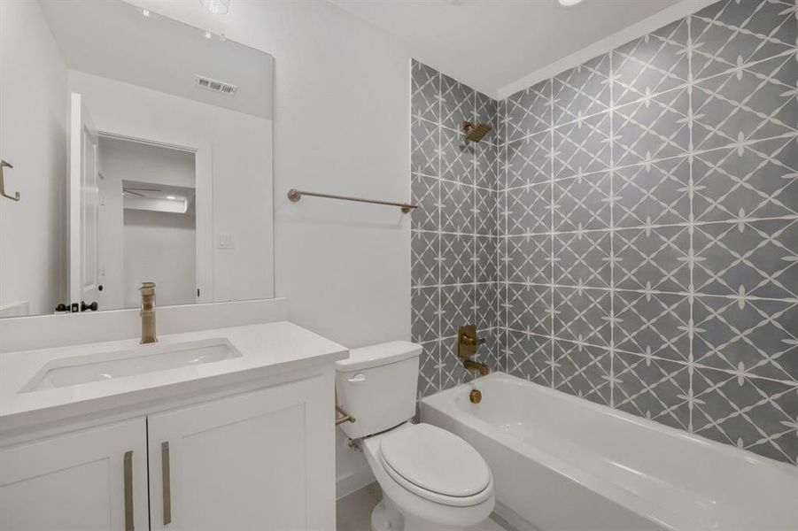 Bathroom featuring patterned wall tile, a white vanity with an integrated sink, a full-width mirror, and brass-finish fixtures Bathroom featuring patterned wall tile, a white vanity with an integrated sink, a full-width mirror, and brass-finish fixtures