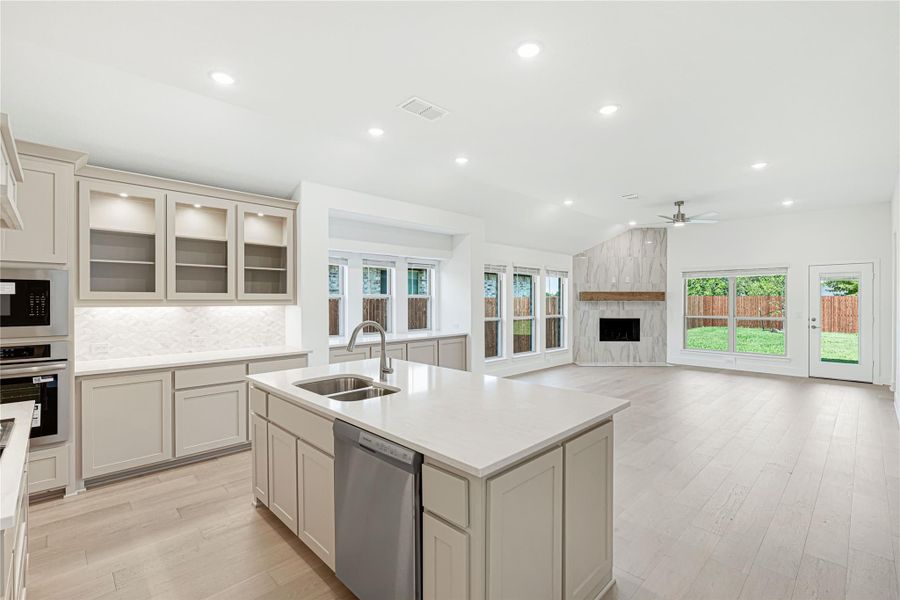 Open kitchen with gray cabinets, center island with sink, and connected living room with fireplace
