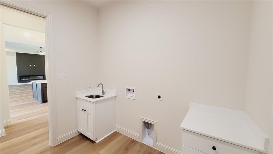 Dedicated laundry space featuring a utility sink with a stainless steel faucet, white shaker cabinetry, and a white countertop