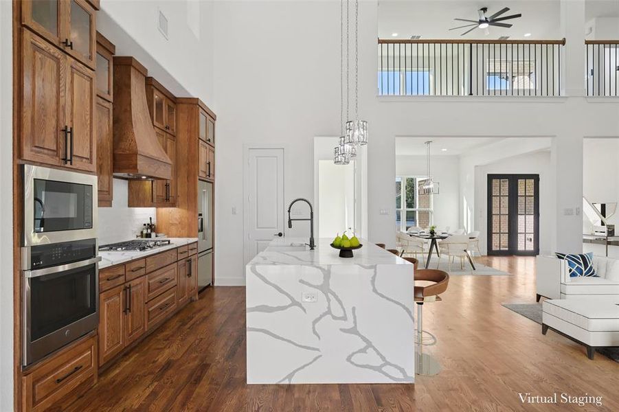 Kitchen with brown cabinetry, light stone countertops, open floor plan, a kitchen breakfast bar, and a towering ceiling