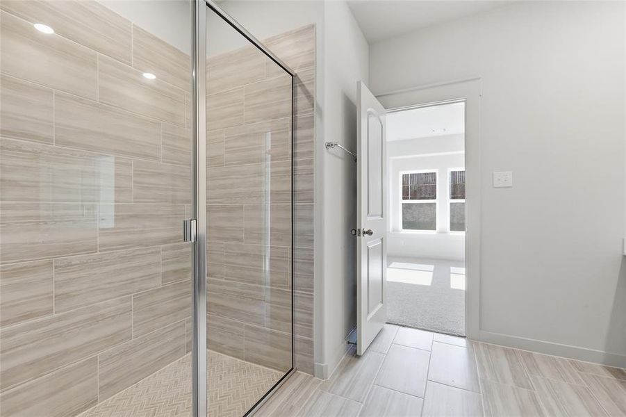Walk-in shower featuring light-toned tile walls, a herringbone pattern tile floor, and a clear glass enclosure