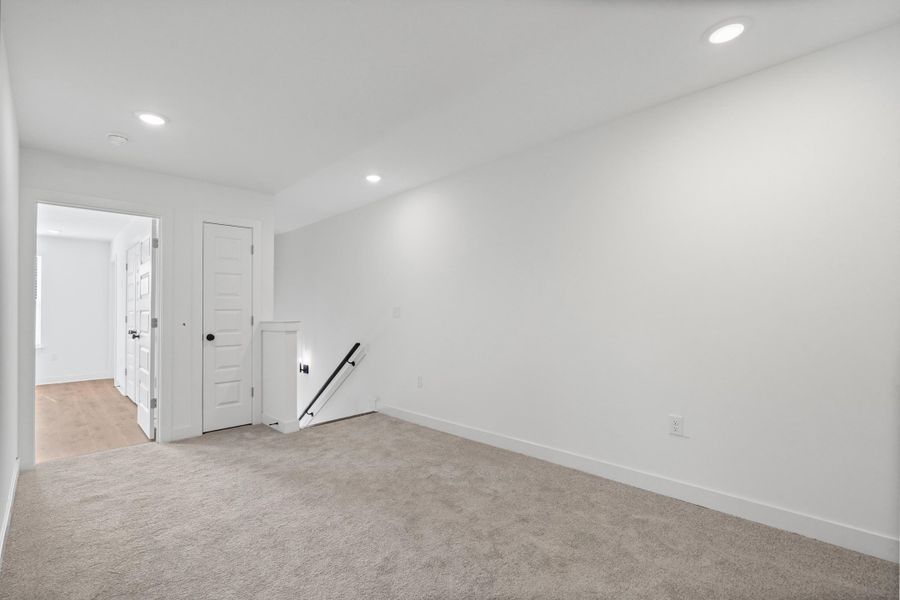 Plush carpeting, recessed lighting, white interior doors, and a black metal handrail