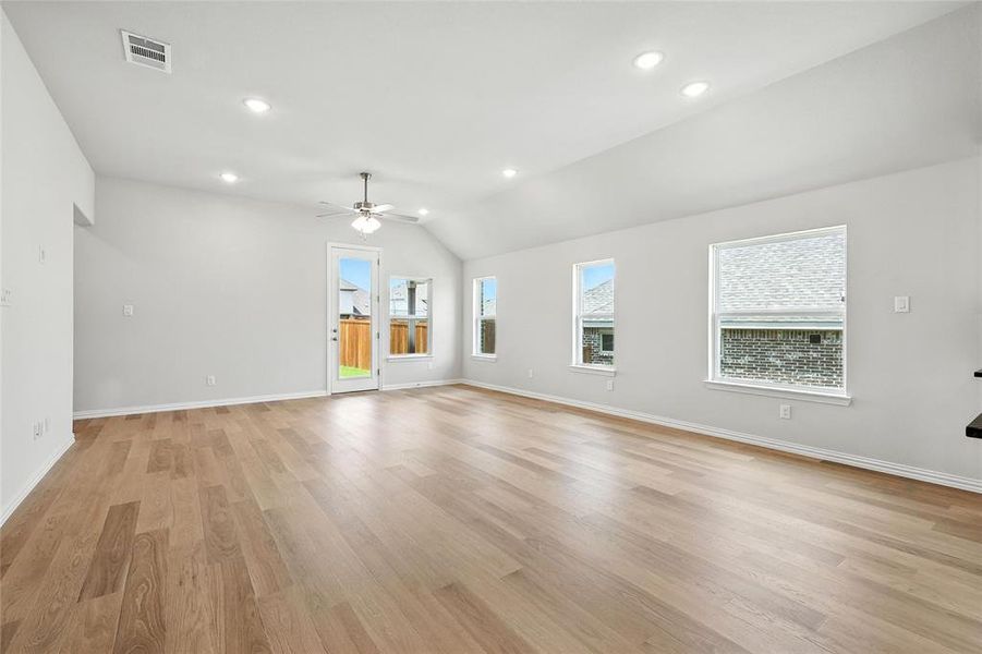 Unfurnished living room with a ceiling fan, light wood finished floors, lofted ceiling, and recessed lighting Unfurnished living room with a ceiling fan, light wood finished floors, lofted ceiling, and recessed lighting