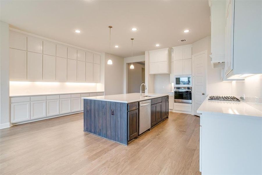 Kitchen featuring appliances with stainless steel finishes, white cabinetry, light wood-type flooring, and a kitchen island with sink