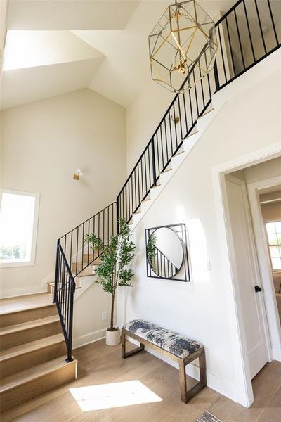 Vaulted entry with wood-finish flooring, a modern geometric chandelier, and black metal stair railing