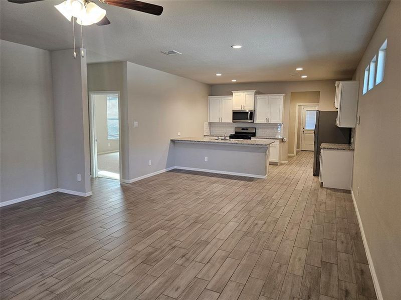 Kitchen with white cabinetry, open floor plan, stainless steel appliances, granite counters, backsplash and wood looking tiled floors.