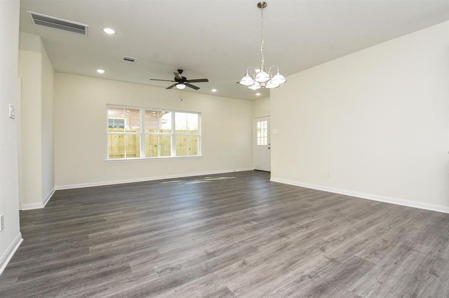 Empty room with gray flooring, tan walls, ceiling fan, window, and a hanging light fixture.