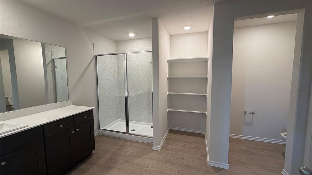 Bathroom featuring a dual vanity with dark wood cabinetry and white countertops, a glass-enclosed shower, built-in shelving, and wood-finish flooring