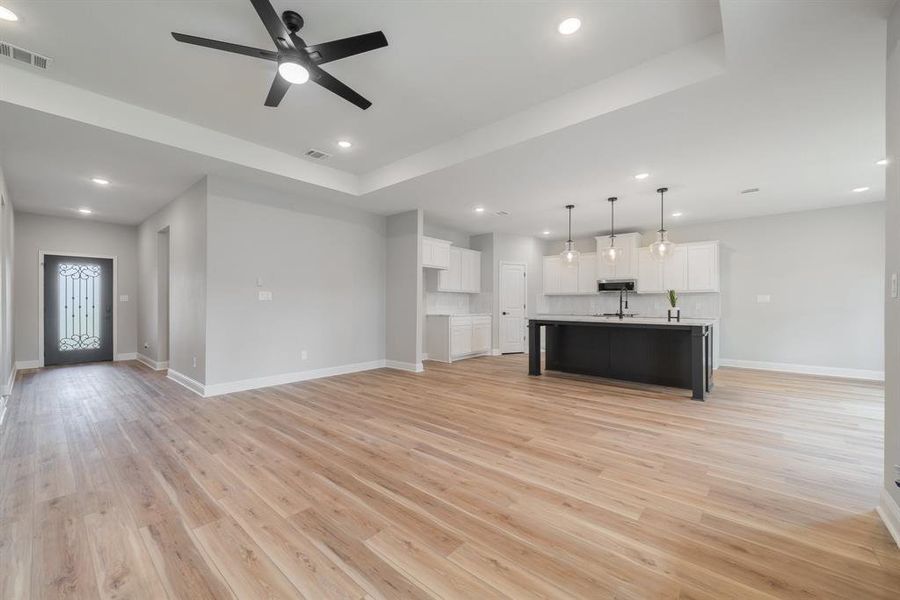 Unfurnished living room featuring ceiling fan, a raised ceiling, and light hardwood / wood-style flooring