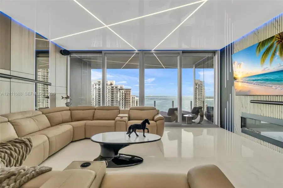 Living space featuring large-format tile flooring, linear ceiling lighting, floor-to-ceiling glass sliding doors, wood-finish wall paneling, and an integrated linear fireplace Living space featuring large-format tile flooring, linear ceiling lighting, floor-to-ceiling glass sliding doors, wood-finish wall paneling, and an integrated linear fireplace