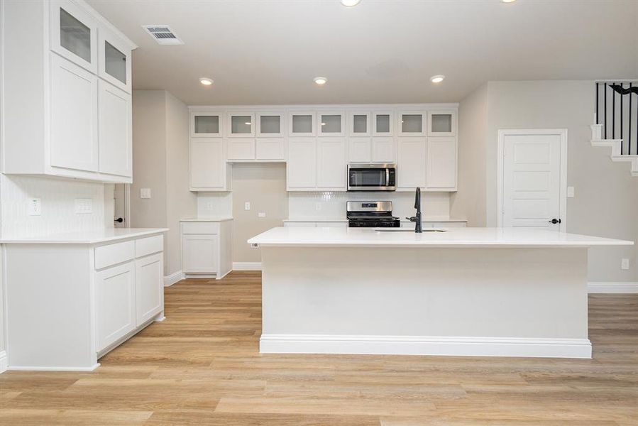 Kitchen featuring decorative backsplash, recessed lighting, glass insert cabinets, white cabinets, and light wood-style floors