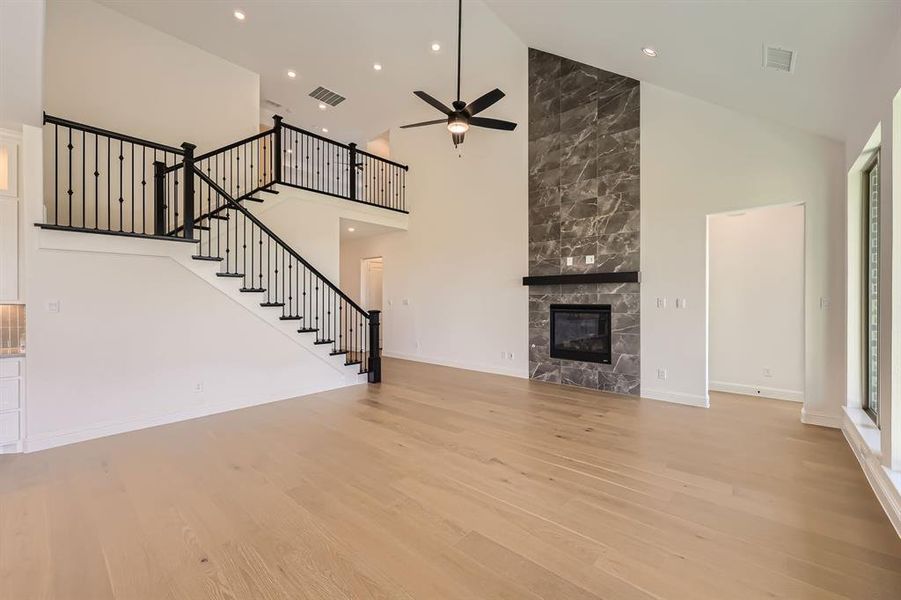 Living room with high vaulted ceiling, a tile fireplace, iron spindle staircase, ceiling fan, and light hardwood / wood-style flooring