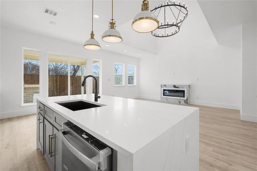 Kitchen with light wood finished floors, stainless steel dishwasher, light stone counters, a kitchen island with sink, and open floor plan Kitchen with light wood finished floors, stainless steel dishwasher, light stone counters, a kitchen island with sink, and open floor plan