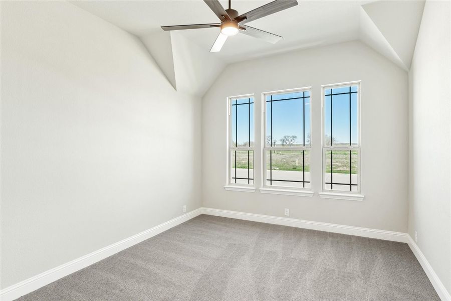 Empty bedroom with vaulted ceiling, ceiling fan, gray carpet, and three windows with outdoor views Empty bedroom with vaulted ceiling, ceiling fan, gray carpet, and three windows with outdoor views