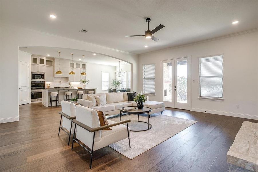 Living room featuring fireplace with stone surround, crown molding, ceiling fan, engineered wood flooring, 10 ft ceilings and 8 ft doors