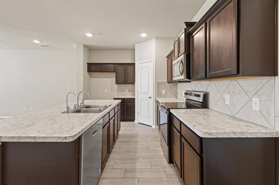 Kitchen featuring appliances with stainless steel finishes, dark brown cabinetry, light countertops, a center island with sink, and recessed lighting Kitchen featuring appliances with stainless steel finishes, dark brown cabinetry, light countertops, a center island with sink, and recessed lighting