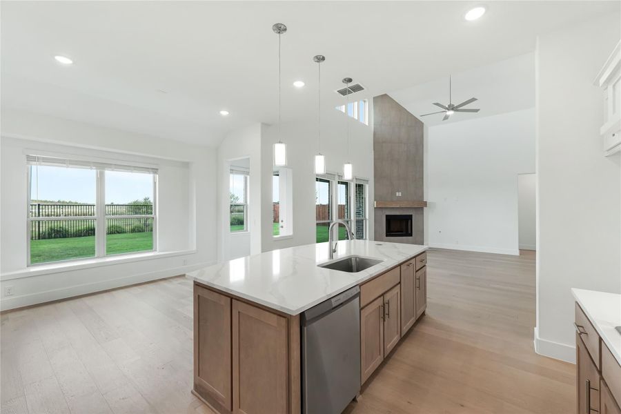 Open-concept kitchen with large island, quartz countertop, and sink, open to living area with fireplace and high ceilings