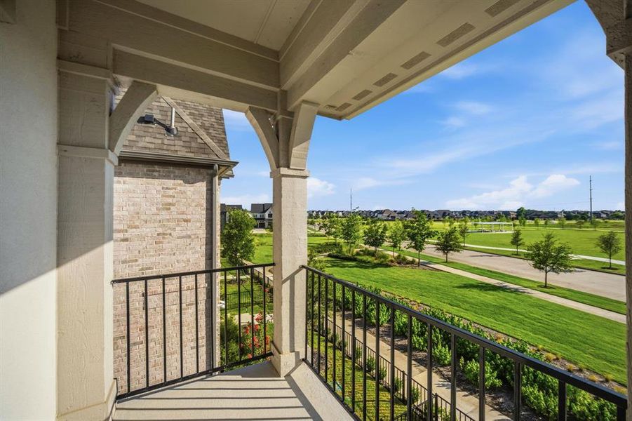 Covered balcony off the primary bedroom, featuring decorative columns, an arched ceiling, and black wrought iron railing