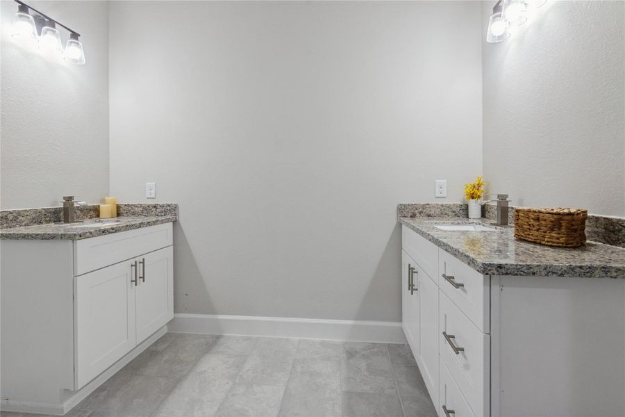 The primary bathroom with dual white vanities featuring granite countertops. The space is well-lit with stylish light fixtures.