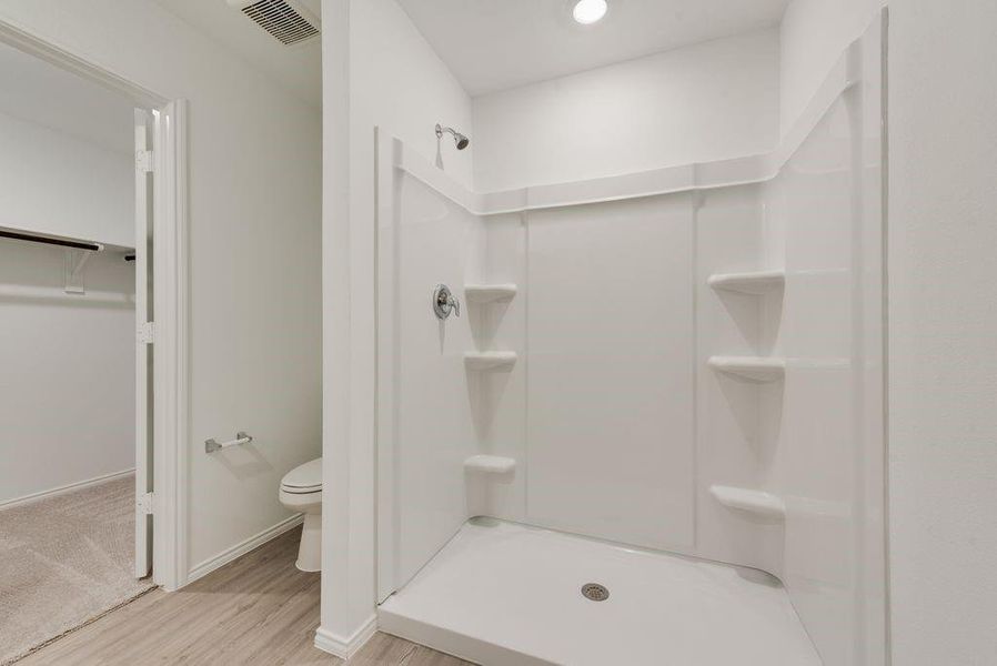 Bathroom with visible vents, toilet, wood finished floors, a spacious closet, and a shower stall