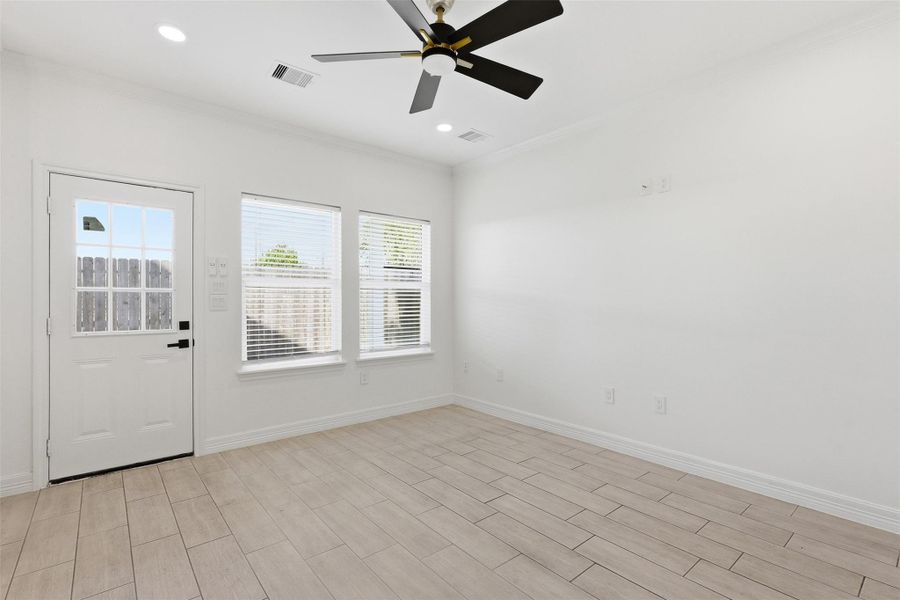 Open living area bathed in natural light through large windows, featuring ceiling fan and light wood look floors.