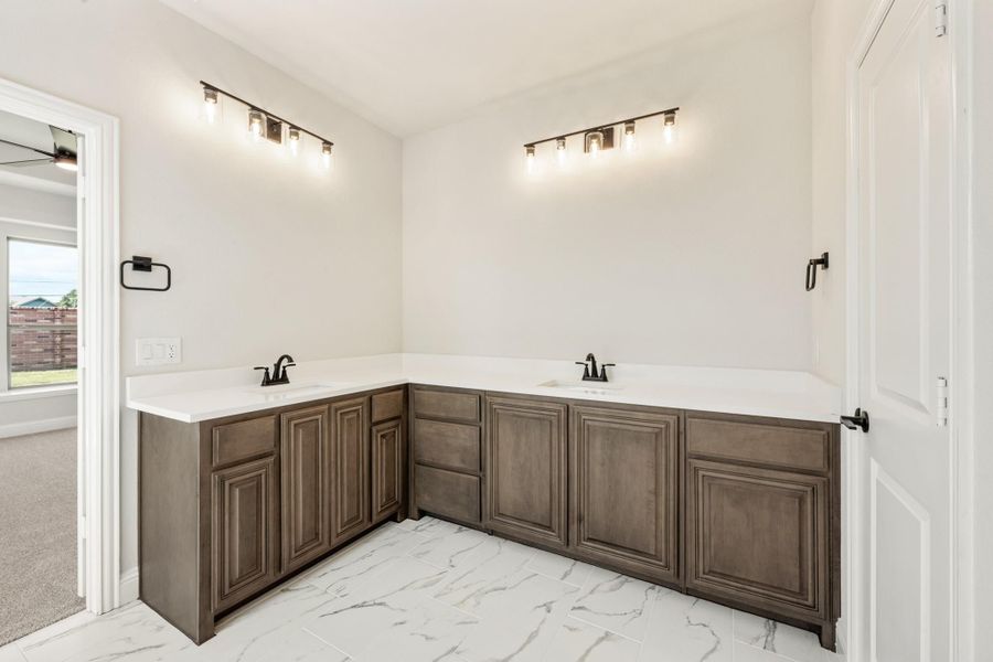 Bathroom with L-shaped double vanity, dark wood cabinets, white countertops, and marble tile floors