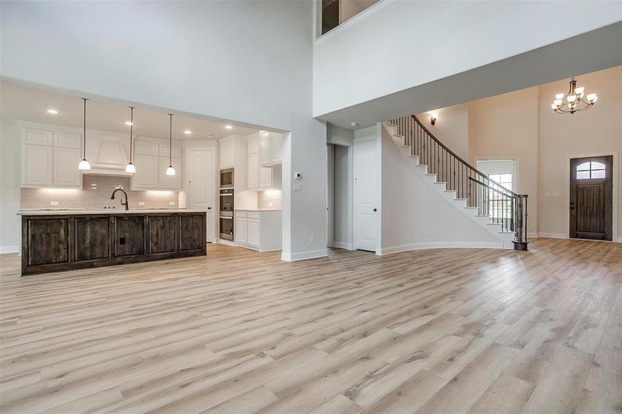 Unfurnished living room with sink, a chandelier, light hardwood / wood-style flooring, and a towering ceiling