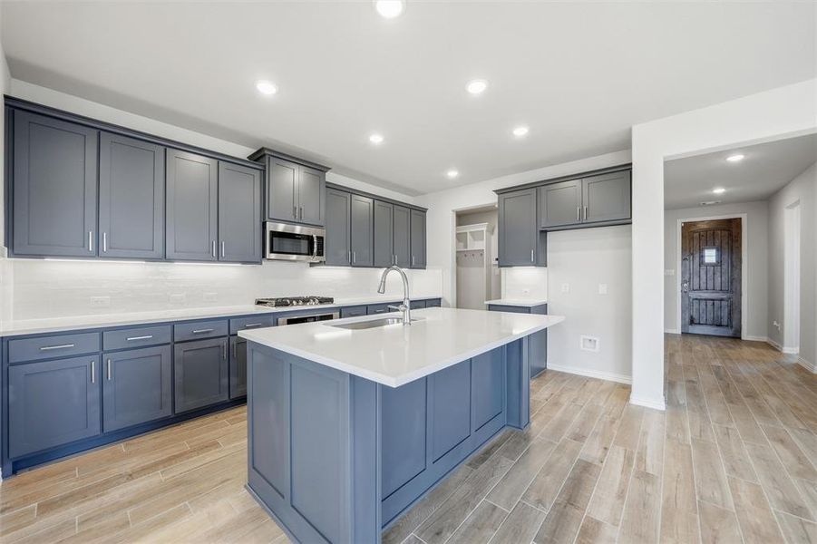 Kitchen featuring wood finish floors, recessed lighting, an island with sink, decorative backsplash, and appliances with stainless steel finishes Kitchen featuring wood finish floors, recessed lighting, an island with sink, decorative backsplash, and appliances with stainless steel finishes