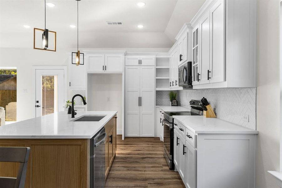 Kitchen with light stone countertops, sink, hanging light fixtures, white cabinets, and appliances with stainless steel finishes