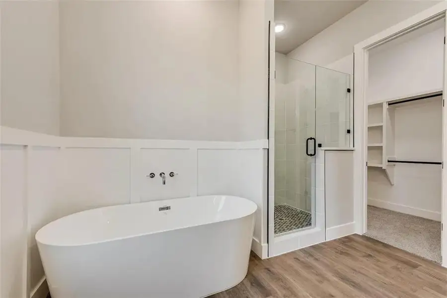 Full bathroom with a stall shower, a spacious closet, wood finished floors, a freestanding bath, and a decorative wall