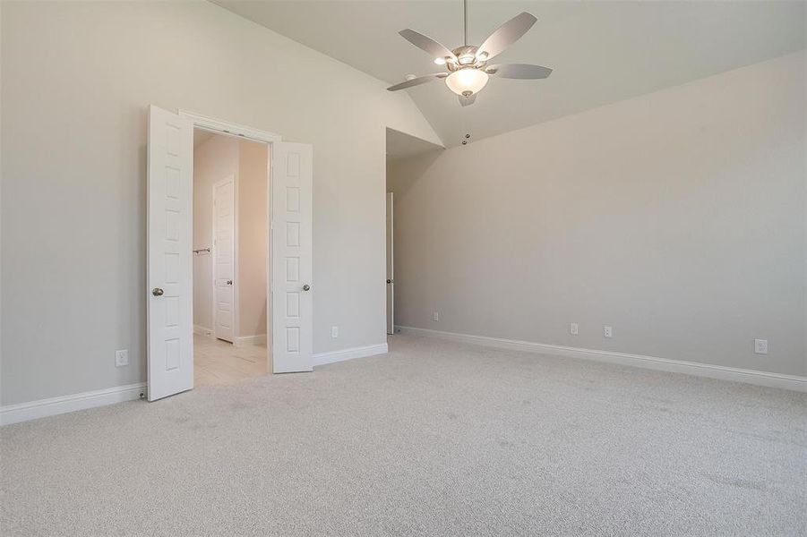 Unfurnished bedroom featuring ceiling fan, vaulted ceiling, and light colored carpet