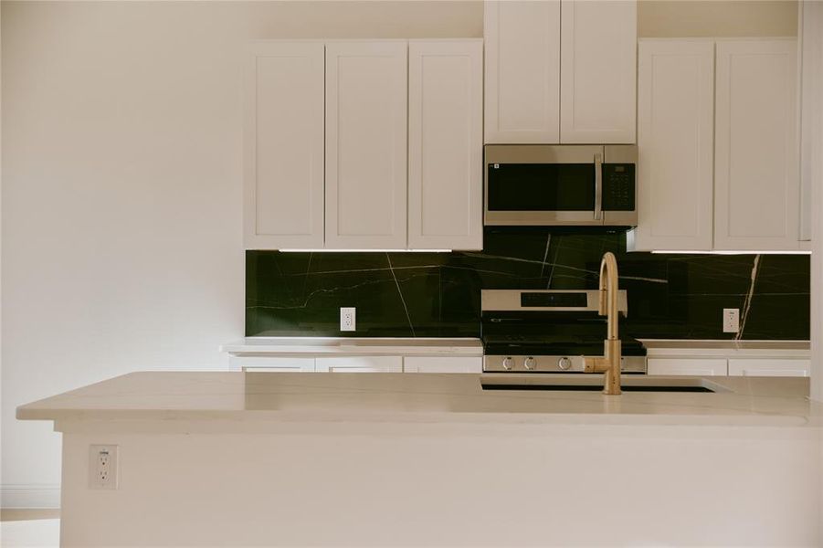 Kitchen with appliances with stainless steel finishes, white cabinetry, and tasteful backsplash