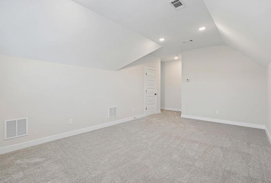 Carpeted room with sloped ceilings, recessed lighting, and a paneled door