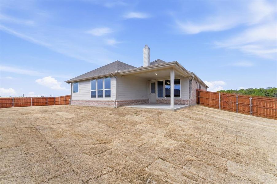 Back of house featuring brick siding, a fenced backyard, a chimney, and a patio area