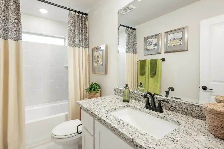 Bathroom with granite countertop vanity, white tub-shower combo, and cream curtains