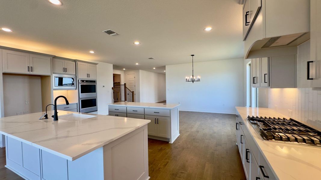 Kitchen featuring dark wood-style flooring, stainless steel appliances, backsplash, light stone countertops, and decorative light fixtures