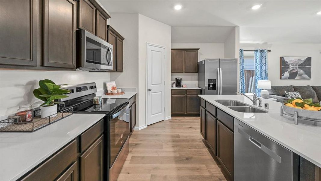 Kitchen with stainless steel appliances, dark wood finish cabinetry, open floor plan, light wood-style flooring, and recessed lighting