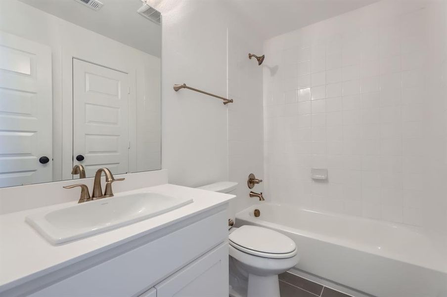 Full bathroom with vanity, toilet, tile patterned floors, and tiled shower / bath