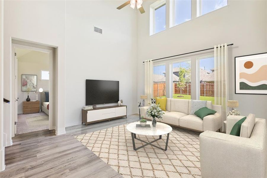 Living room with ceiling fan, light hardwood / wood-style flooring, a towering ceiling, and a healthy amount of sunlight