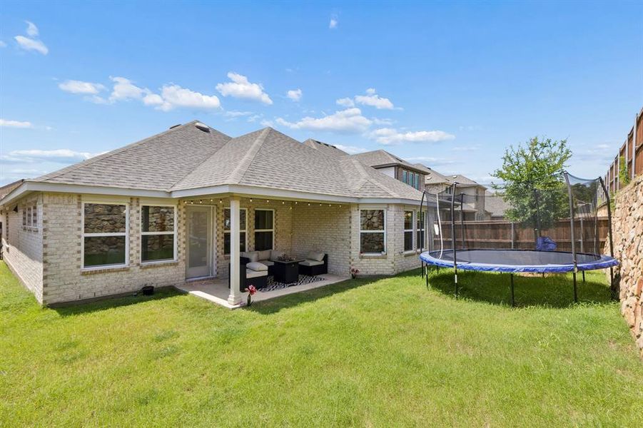 Expansive backyard featuring a covered patio, a light-colored brick exterior, multiple windows, and a privacy fence