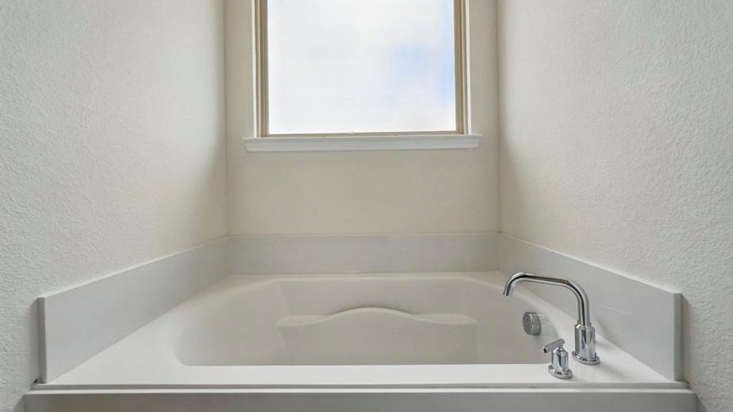 Built-in soaking tub with polished chrome fixtures and a frosted window
