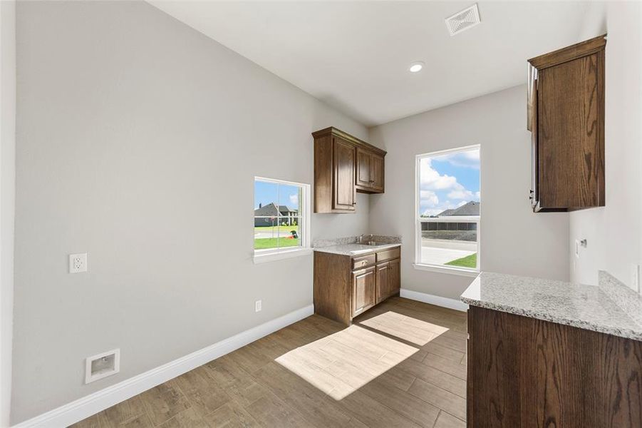 Kitchen featuring dark brown cabinets, light stone counters, and dark hardwood / wood-style floors